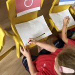 Proposta pendent de confirmar: Nens d'I4 jugant al joc de les cadires per practicar els traços de Ludilletres a l'aula.